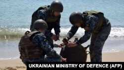 Українські військові знешкоджують морську міну, викинуту на берег штормом, під час масштабного вторгнення Росії до України. Фото оприлюднило Міноборони України 16 травня 2022 року