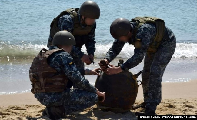 Українські військові знешкоджують морську міну, викинуту на берег штормом, під час масштабного вторгнення Росії до України. Це фото оприлюднило Міноборони України 16 травня 2022 року