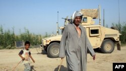 فلاح عراقي وابنه يمران قرب عربة همفي أميركية جنوب بغداد