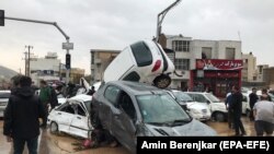 IRAN -- People stand near destroyed cars after a flood hit the city of Shiraz, March 25, 2019