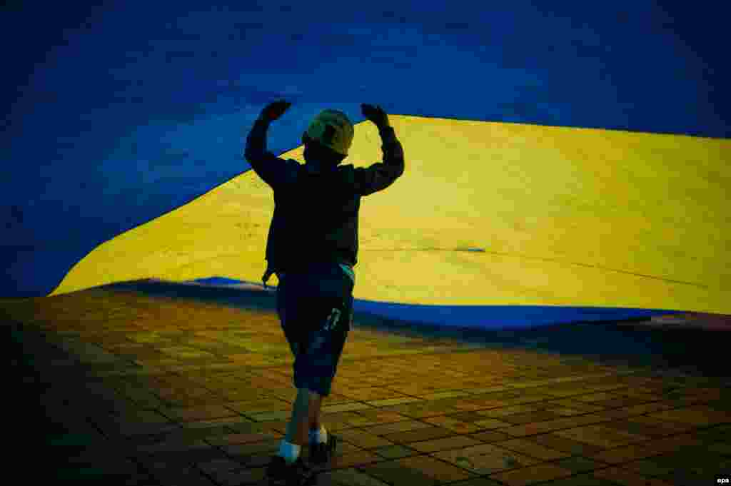 A child refugee plays under the Ukrainian flag during a rally on the sidewalk at the entrance to the parliament in Kyiv on June 5. (epa/Roman Pilipey)