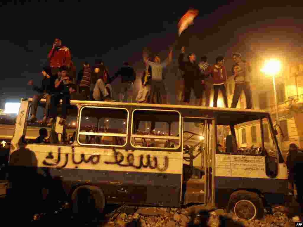 Protesters celebrate on a wrecked bus used as a barricade with "Let Mubarak Fall" scrawled on it in Tahrir Square.