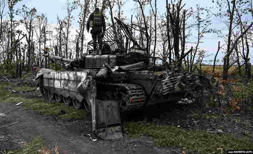 Militari ucraineni inspectează un tanc rusesc distrus în timpul contraofensivei Forțelor Armate ale Ucrainei la periferia orașului Izium, regiunea Harkov, pe 11 septembrie 2022.