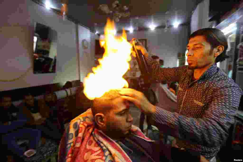 Palestinian barber Ramadan Odwan styles and straightens the hair of a customer using fire at his salon in Rafah in the southern Gaza Strip. (Reuters/Ibraheem Abu Mustafa)