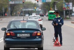 Карантин кезінде көшеде жүрген көлікті тоқтатып, тексеріп тұрған полиция қызметкері. Алматы, 14 сәуір 2020 жыл.
