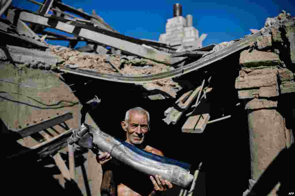 Një burrë ukrainas mban një pjesë të një rakete në shtëpinë e tij të shkatërruar pas granatimeve në fshatin Olenivka, në jug të fortesë e rrethuar rebele të Donetskut.