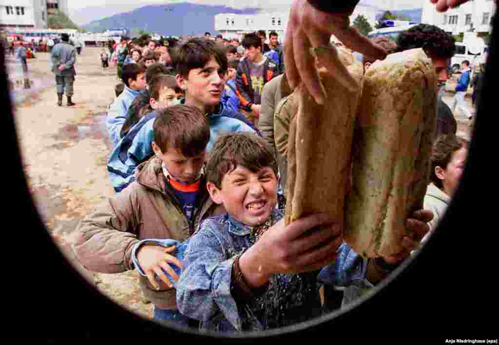 An ethnic Albanian refugee child grimaces as he reaches out for bread in the center of Kukes, a northern Albanian border town, on April 20 1999.