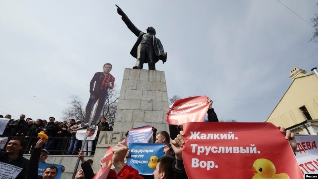 Opposition supporters hold posters and a cutout figure depicting Prime Minister Dmitry Medvedev during a rally in front of a monument of Soviet state founder Vladimir Lenin in Vladivostok on March 26, 2017.