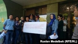 Участники объединения проблемных заемщиков ипотечных кредитов «Обеспечьте народ жильем» стоят с плакатом у здания городского суда. Алматы, 10 мая 2017 года.