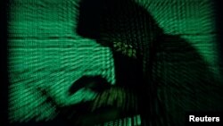 A hooded man holds a laptop computer as cyber code is projected - generic