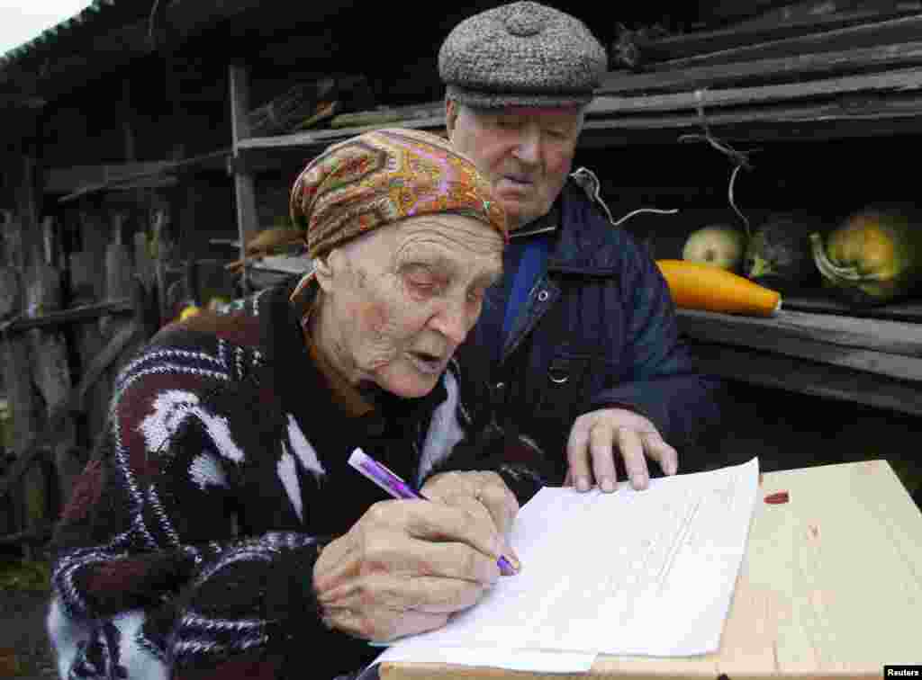 A woman signs a form to receive a ballot before casting her vote in a portable ballot box near her house in the village of Skuraty.