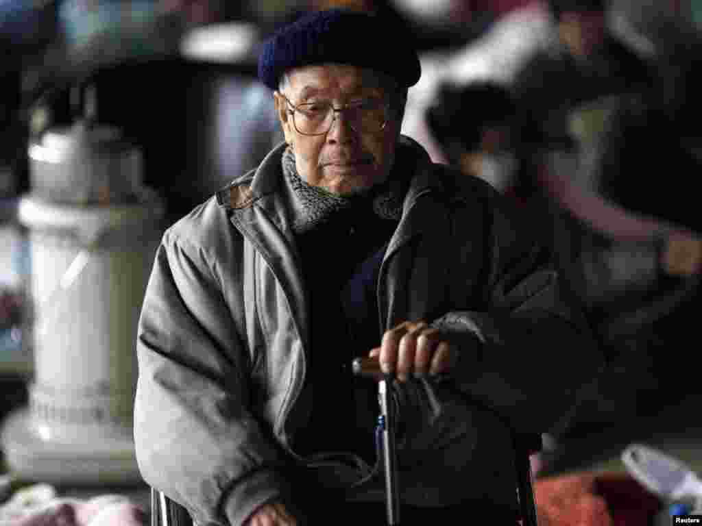 A survivor keeps himself warm by a fire at an emergency shelter in Otsuchi on March 16