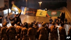 Supporters of the Iran-backed militant group hold the flags of Shiite Hezbollah and Amal Movement groups, as they stand in front of Lebanese army soldiers who divided between them and the anti-government protesters after a clashes erupted between them, in Beirut, Lebanon, early M