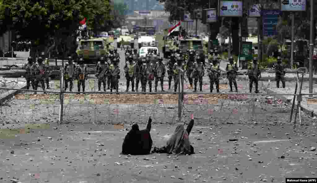 Egyptian supporters of deposed President Muhammad Morsi sit in front of barbed-wire fencing set up to block access to the headquarters of the Republican Guard in Cairo. (AFP/Mahmud Hams)