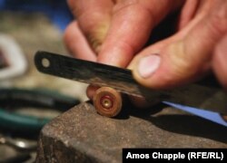 The jeweler saws off the cap of a bullet casing.