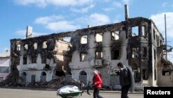 People walk past a destroyed building in the town of Vuhlehirsk, north-east from Donetsk, March 8, 2015