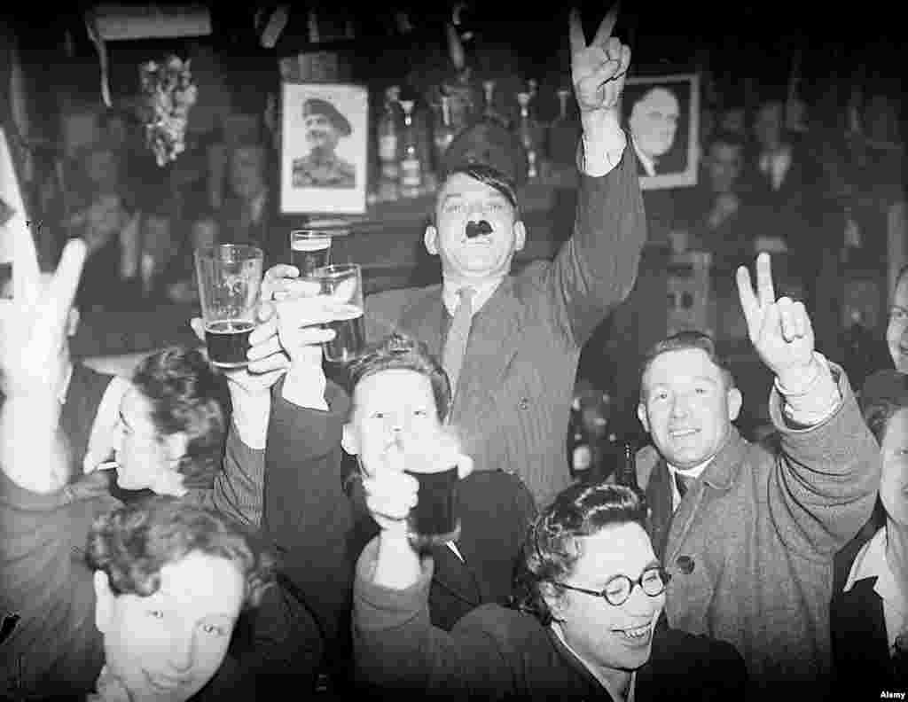Londoners, including a man with his nostrils stuffed with Hitler-like bristles, gleefully sink beers in a pub in the Lambeth part of London.