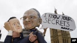 Демонстрант од организацијата Аваз со маска на медиумскиот магнат Рупер Мурдок држи кукла со ликот на британскиот премиер Дејвид Камерон пред Парламентот во Лондон на 13 јули 2011 година.