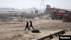 Employees of the Iraqi state-run South Oil Company (SOC) walk near a damaged pipeline in Al-Basrah province in December.