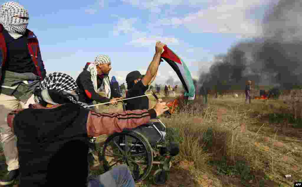 A picture taken on December 15 shows wheelchair-bound Palestinian demonstrator Ibrahim Abu Thurayeh waving a Palestinian flag amid smoke from flaming tires during a protest along the Gaza-Israel border against the U.S. recognition of Jerusalem as Israel's capital. (AFP)