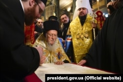   The Ecumenical Patriarch Bartholomew signs the tomos of autocephaly for the Orthodox Church of Ukraine (ECP). The Metropolitan of Kiev and all of Ukraine, Epiphanius, stands to his left. Istanbul, January 5, 2019 