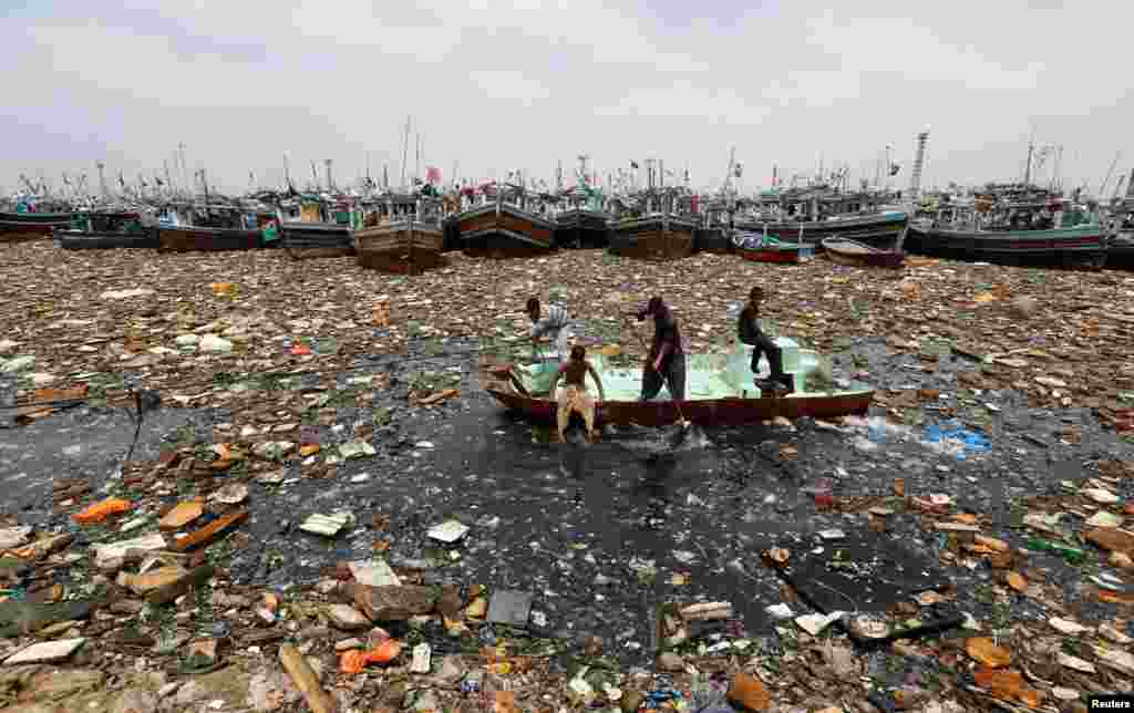 Boys aboard an abandoned boat collect recyclable items through polluted waters in front of fishing boats at Fish Harbor in Karachi, Pakistan. (Reuters/Akhtar Soomro)