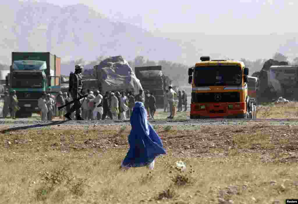 An Afghan woman (center) walks past as Afghan security forces secure the site of burning NATO supply trucks after a Taliban attack in the Behsud district of Nangarhar Province on June 9. (Reuters/Parwiz)