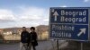 A couple walks past a traffic sign pointing toward the capitals of Serbia and Kosovo.