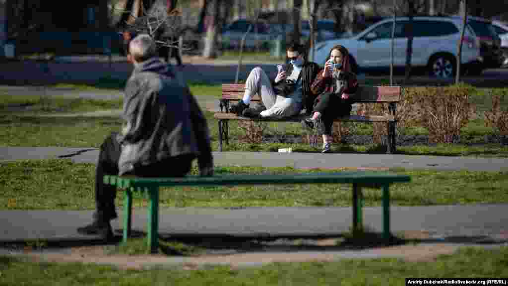 Чоловік та дівчата у масках сидять на лавочках у Оболонському районі, Київ, 7 квітня 2020 року
