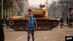 An opposition supporter plays football next to a Republican Guard tank deployed outside the presidential palace in Cairo.