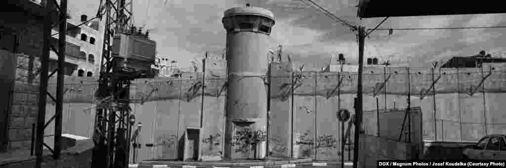 Josef Koudelka, A-Ram, Ierusalimul de est, 2010 &nbsp; Josef Koudelka face din zidul separator caracterul epic central al lucrării sale fotografice. Grafica, fotografiile lui panoramice, redau sensul acestui peisaj arhaic, impactul zidului asupra lui și realitatea dureroasă a drumul divizat de zid. 