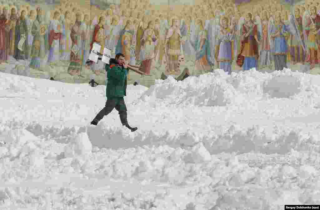 In the Ukrainian capital, Kyiv, a city worker prepares to clean up the heavy snow in front of the Mikhailovsky Cathedral&#39;s frescos on March 26.