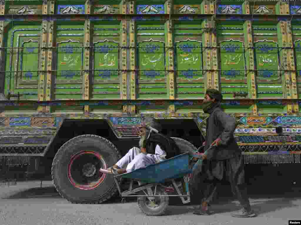 A teenage boy uses a wheelbarrow to push an elderly Pashtun man past a supply truck in Pakistan after traffic was halted at the Pakistan-Afghanistan border crossing in Chaman. (REUTERS/Naseer Ahmed)