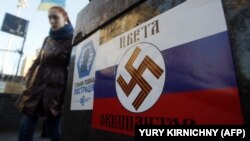 Дівчина проходить повз плакат із нацистською свастикою на російському прапорі та написом «Кольори окупантів» у столиці України. Київ, майдан Незалежності, 12 березня 2014 року