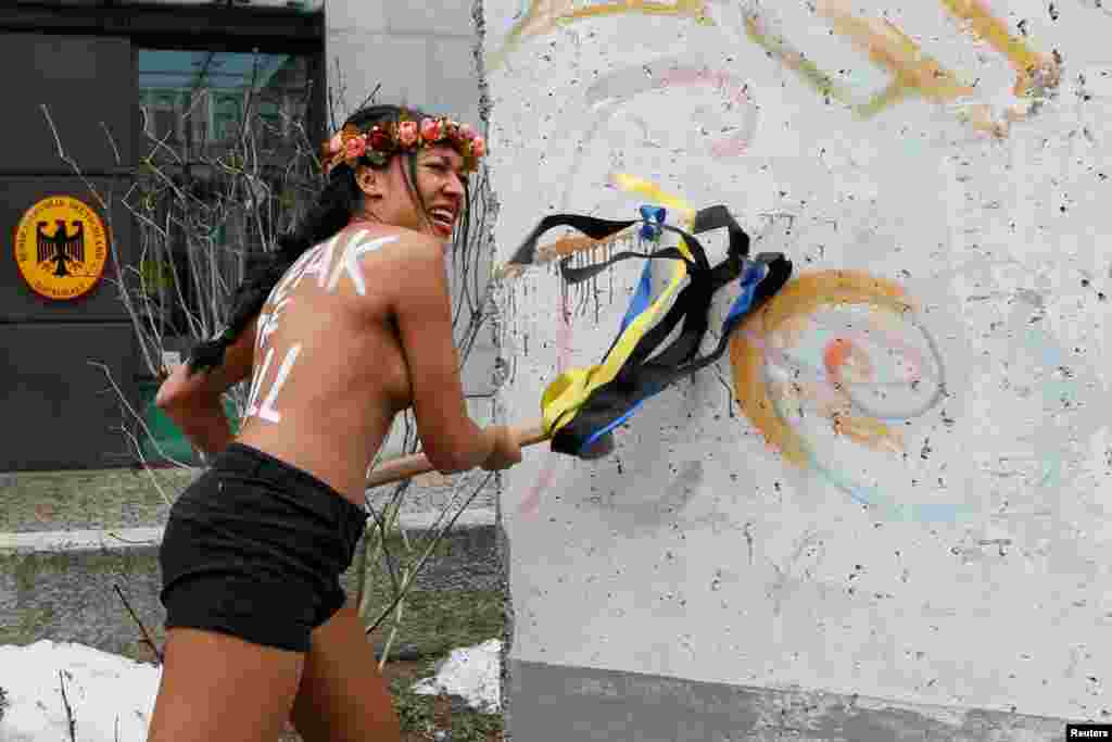 Aýallaryň hukuklaryny gorýan Femen toparynyň çyplaň aktiwist Kiýewde, ÝB-niň ukrainler üçin wiza düzgünine garşy protestde, &nbsp;Berlin diwarynyň german ilçihanasynyň işiginde goýlan bölegini döwmäge synanýar. 24-nji noýabr. (Reuters/Valentyn Ogirenko)