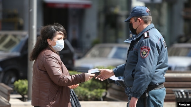 Armenia -- A police officer enforcing a coronavirus lockdown checks a woman's documents, Yerevan, March 25, 2020.