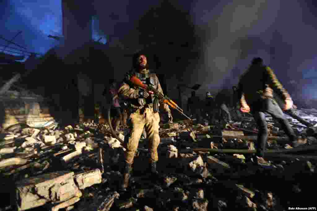 Syrian civil-defense workers (White Helmets) and Turkish-backed Syrian forces search for victims in the aftermath of a car-bomb explosion near a security checkpoint in the town of Azaz, in the north of Aleppo Province near the border with Turkey. (AFP/​Bakr Alkasem)