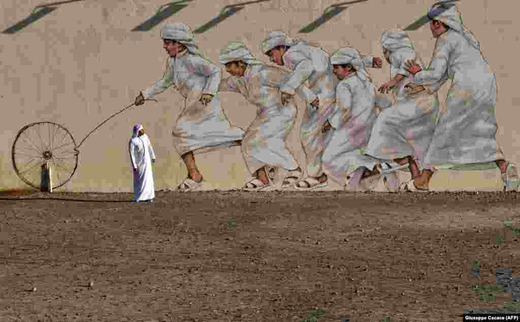 A man walks past a giant mural depicting boys running after a wheel, in Dubai. (AFP/Giuseppe Cacace)