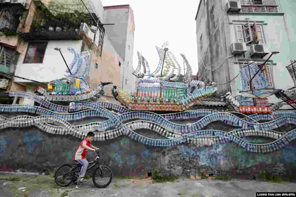 Хлопчик проїжджає на велосипеді повз витвори мистецтва на вулиці в Ханої, В&#39;єтнам, 20 квітня 2020 року. Шістнадцять робіт із матеріалів (таких як пластикові пляшки, бочки та старі колеса) розмістили по вулиці, щоб підвищити обізнаність місцевих жителів про охорону довкілля
