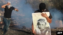 Palestinian protesters run for cover as Israeli forces (unseen) launch tear gas during clashes following a demonstration on November 11 marking the ninth anniversary of the death of Palestinian leader Yasser Arafat, seen in portrait.