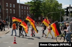 A group of demonstrators opposed to the unveiling carrying German flags. The Lenin monument is visible, covered in a red sheet, in the background.