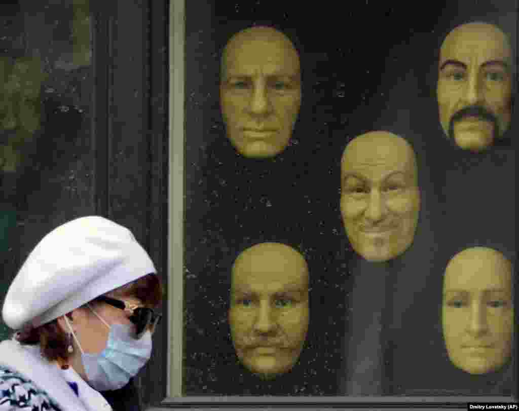 A woman wearing a mask to protect against the coronavirus walks past model faces displayed in a window of a wax museum in St. Petersburg, Russia. (AP/Dmitri Lovetsky)
