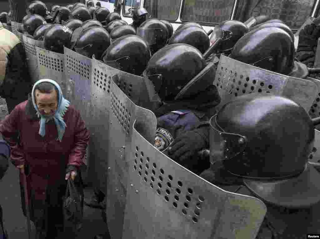 A elderly Ukrainian woman passes by security personnel as they cordon off pro-EU demonstrators near the Ministry of Internal Affairs in Kyiv on December 20. (Reuters/Gleb Garanich)