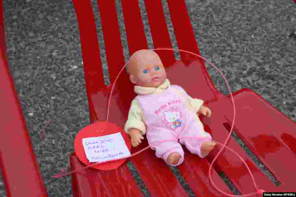 A baby doll rests on a red chair that is one of 643 representing the children who died in the siege.
