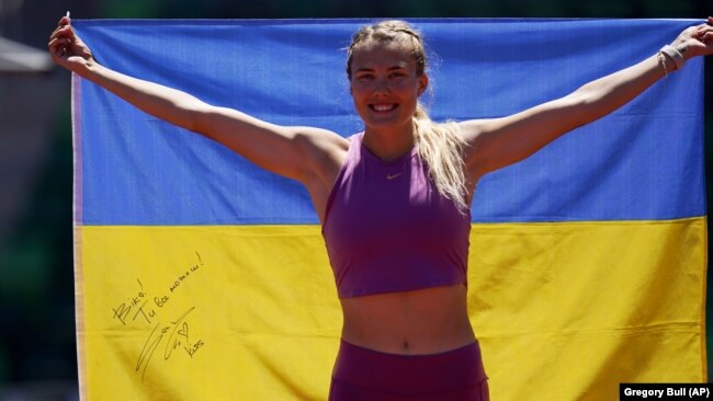 Viktoriya Tkachuk of Ukraine poses for a teammate with a flag signed by the Ukrainian rock band The Hardkiss as she trains before the World Athletics Championships in Eugene, Oregon, on July 14.