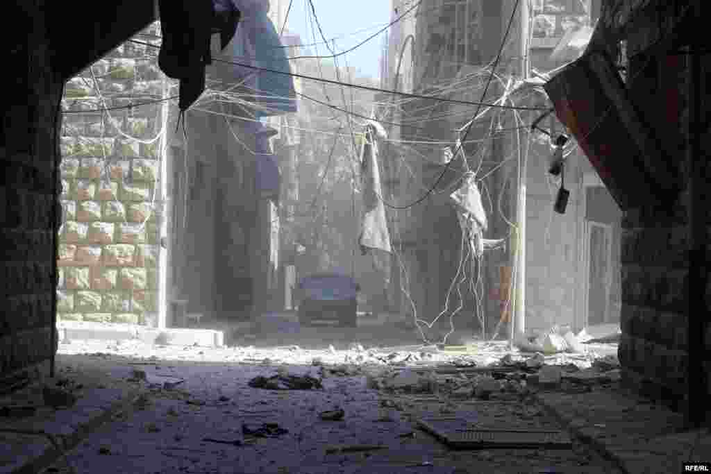 Хәлебнең Бустан әл-Каср бистәсендә бомбалаудан соң таш кисәкләре һәм башка әйберләр белән капланган урам буйлап бер машина бара.