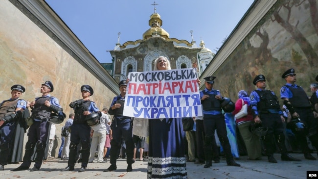 Фото пізнішого періоду. Українка тримає плакат з гаслом «Московський патріархат – це прокляття для України!» під час протесту перед кордоном міліції біля входу до Києво-Печерської лаври. Київ, 13 серпня 2014 року