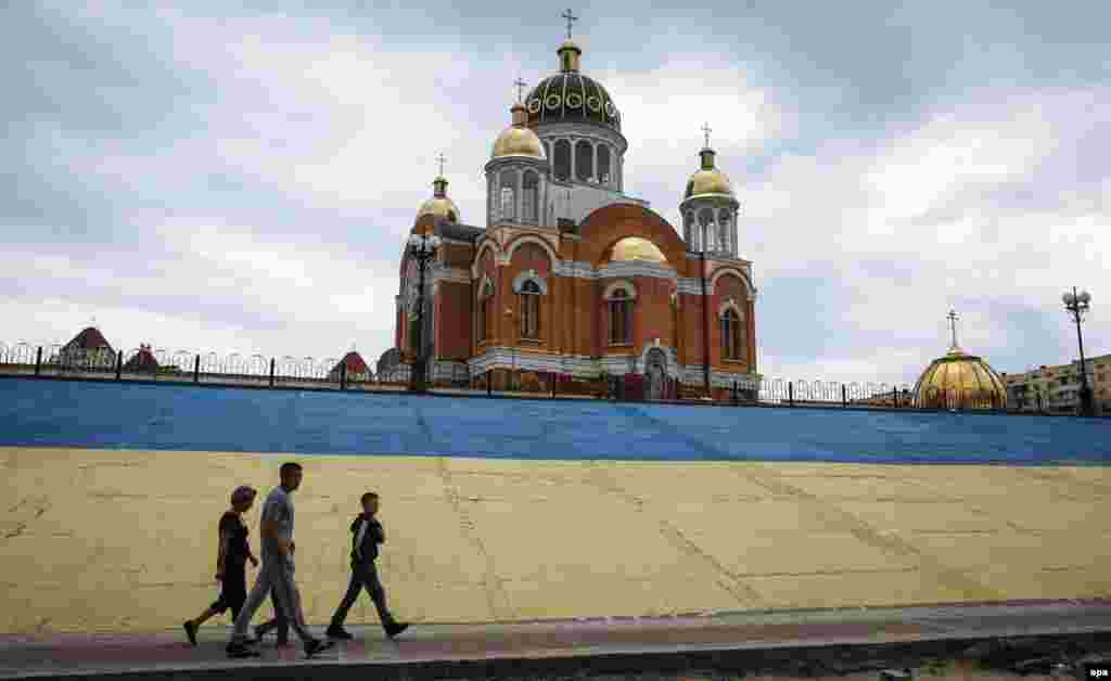 People walk past the Church of the Intercession of the Holy Virgin on a Dnipro River embankment painted in the colors of the Ukrainian national flag in Kyiv on June 26. (epa/Roman Pilipey)