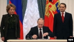 Russia -- President Vladimir Putin (C) signs a law on ratification of a treaty making Crimea part of Russia, during a ceremony in the Kremlin in Moscow, March 21, 2014