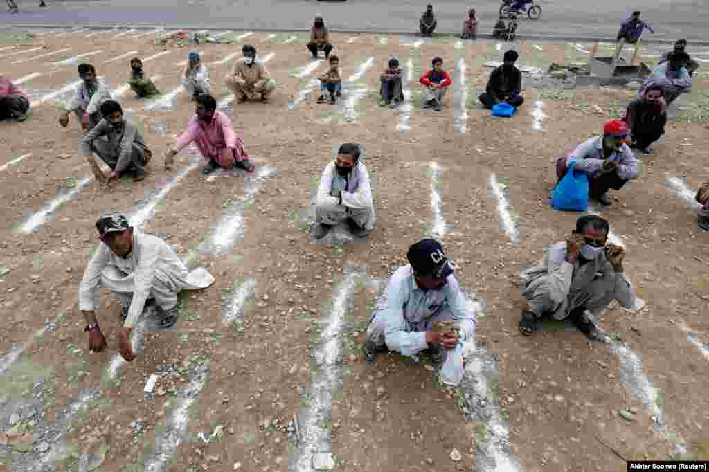 In the Pakistani city of Karachi, chalk lines are used to keep people at a safe distance. These men wait to receive sacks of food from a charity on March 26. Pakistan has shut all markets, public places, and discouraged large gatherings to contain the spread of the coronavirus.